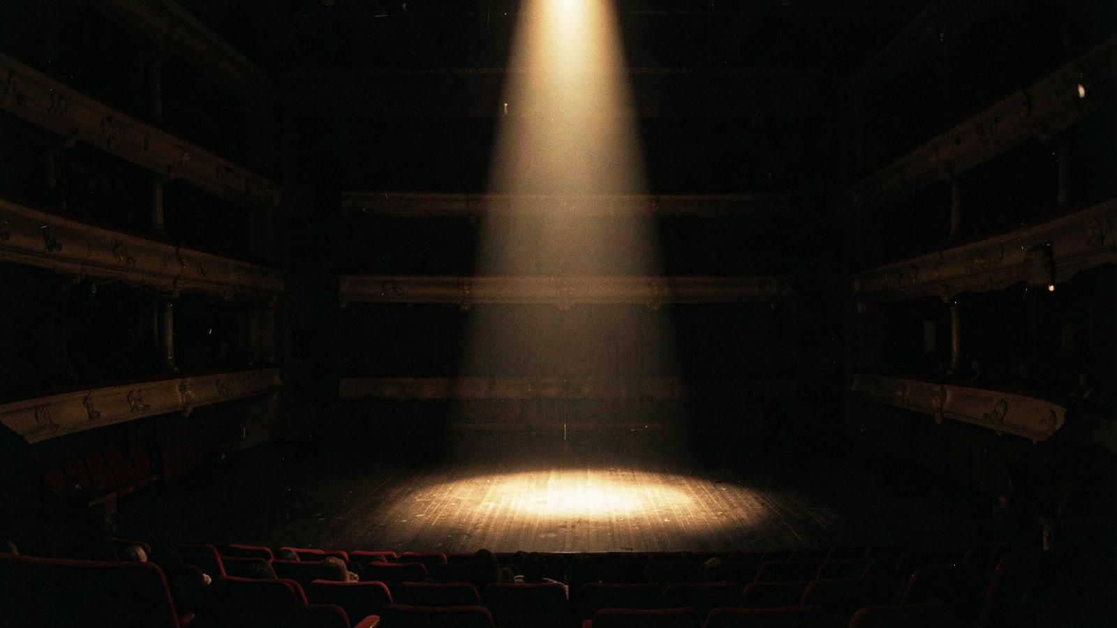 Performer on a dark stage beneath a single spotlight